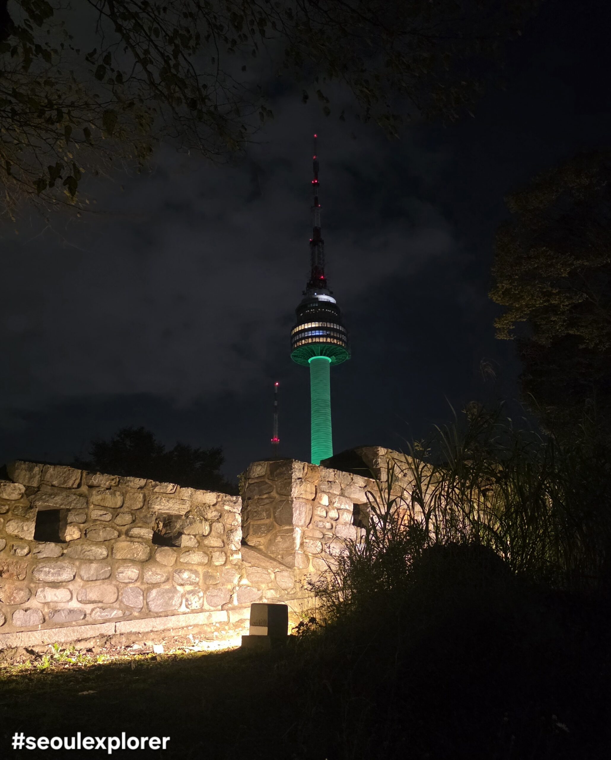 Night view of Namsan Seoul Tower glowing in green behind the ancient fortress wall